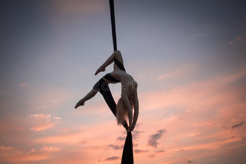 Fit woman in skinny skinny clothes dancing with aerial silk on a sky background, gymnast training on aerial silk. Fit woman in skinny skinny clothes dancing with aerial silk on a sky background, gymnast training on aerial silk