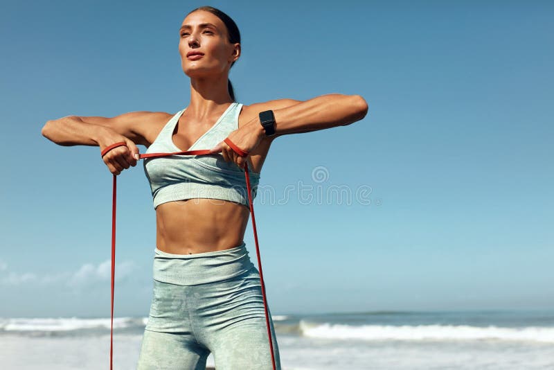 Fitness Girl On Beach Portrait. Stretching Workout With Resistance Loop On Tropical Ocean Background. Sporty Woman With Strong Muscular Body In Fashion Sportswear Training On Summer Vacation. Fitness Girl On Beach Portrait. Stretching Workout With Resistance Loop On Tropical Ocean Background. Sporty Woman With Strong Muscular Body In Fashion Sportswear Training On Summer Vacation.