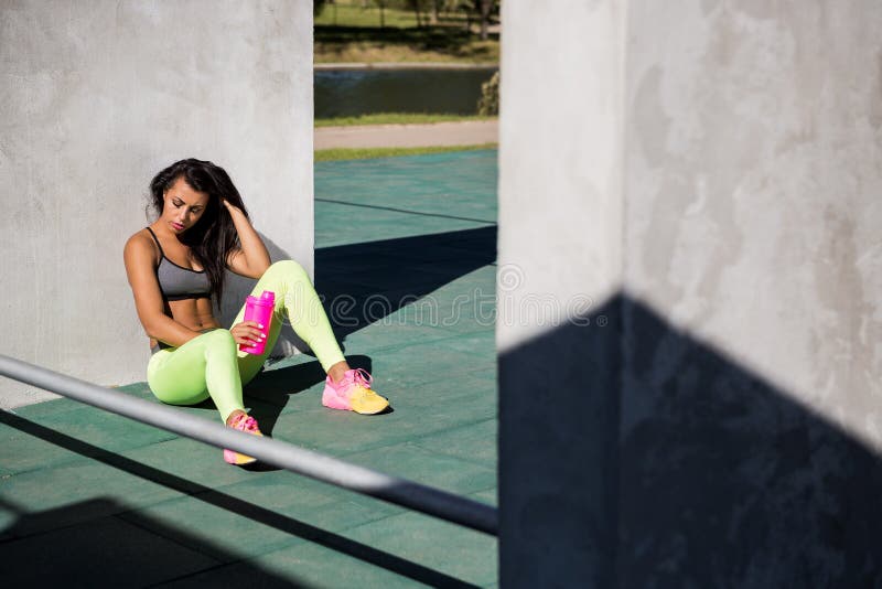 Beautiful young girl with long legs in bright leggings with pretty athlete muscular body sit with protein shaker. Crossfit training urban area street gym city exercise routine healthy lifestyle. Beautiful young girl with long legs in bright leggings with pretty athlete muscular body sit with protein shaker. Crossfit training urban area street gym city exercise routine healthy lifestyle.