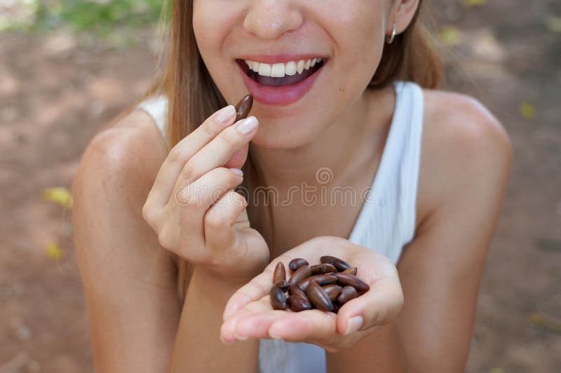 Fitness healthy woman outdoors. Close up of girl eating baru nut seeds in the park. Selective focus on hand picking seeds.