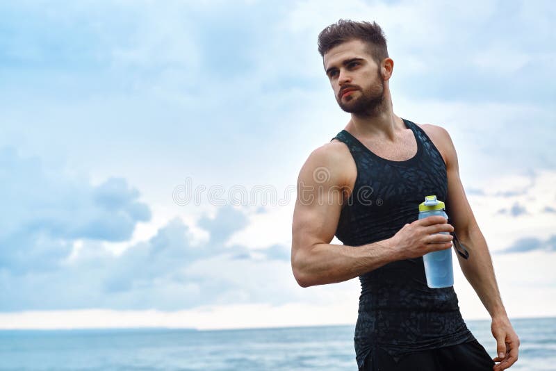 Muscular man holding his water bottle and resting from workout