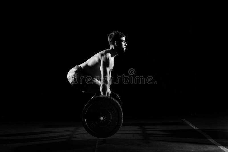 Fitness training. Man doing exercises or training with barbell in dark gym. Fitness training. Man doing exercises or training with barbell in dark gym.