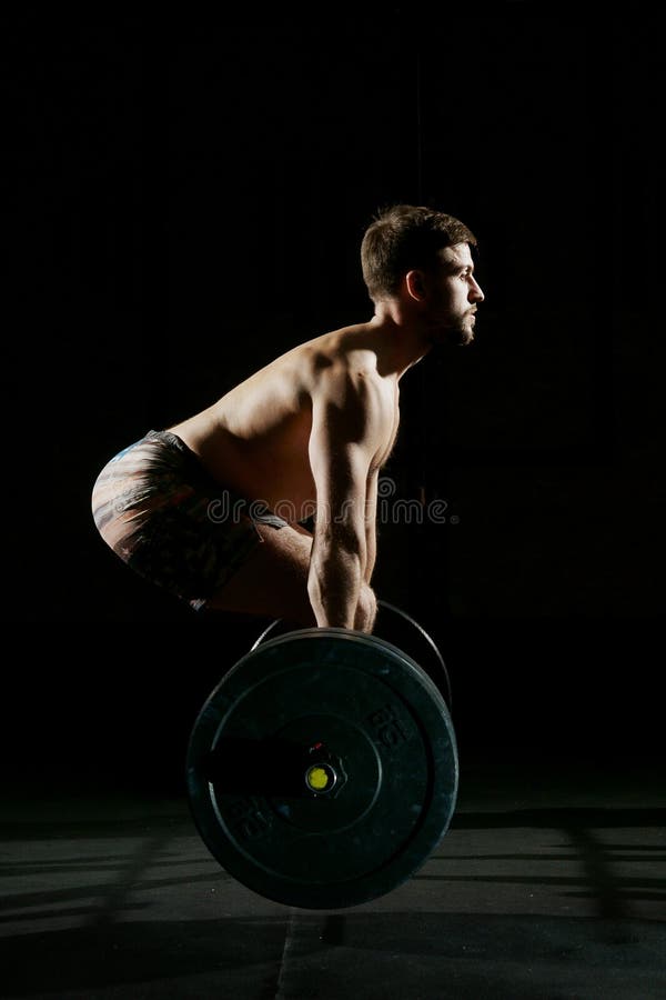 Fitness training. Man doing exercises or training with barbell in dark gym. Fitness training. Man doing exercises or training with barbell in dark gym.