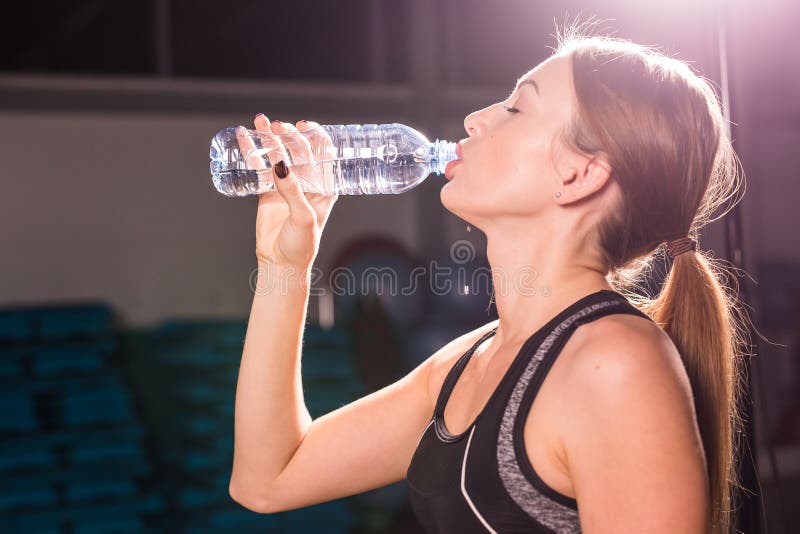 Fitness young woman drinking water in the gym. Muscular woman taking break after exercise