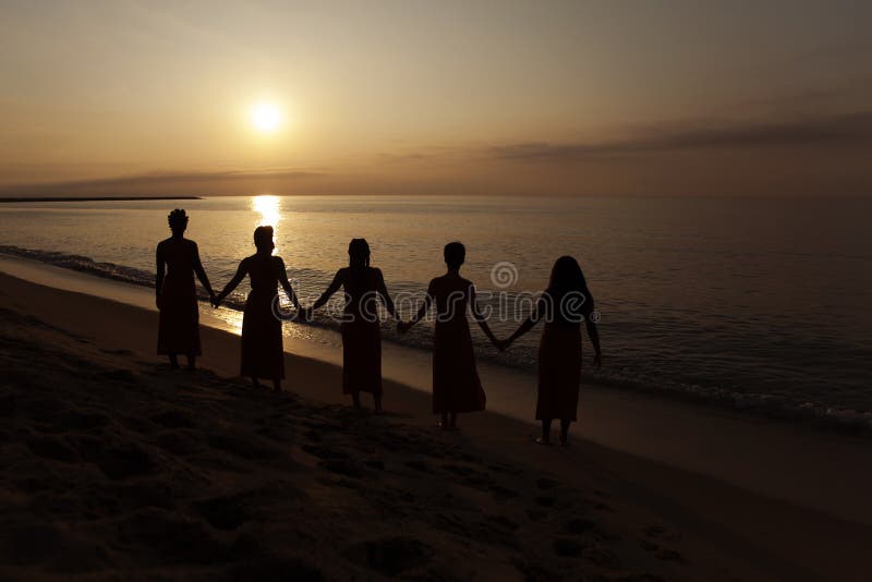 Five black women hold hands looking at the sunrise at the beach. Natural enviorment at Barcelona. Sorority
