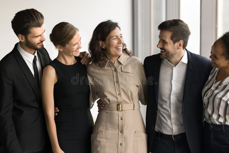 Five business colleagues hugging, stand together in office stock photo