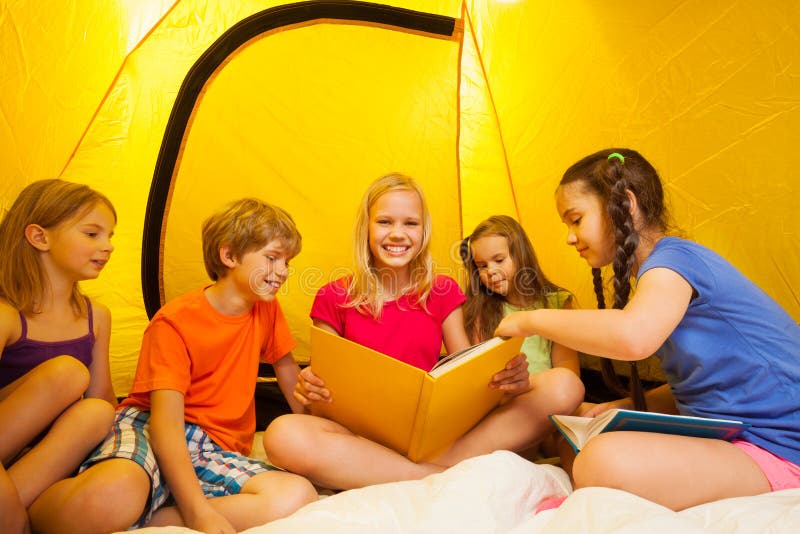 Five funny kids read book inside a yellow tent. Five funny kids read book inside a yellow tent.