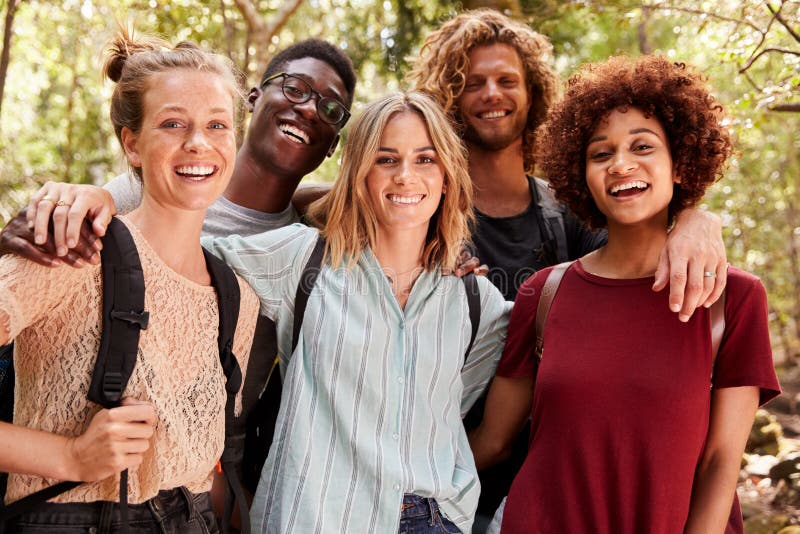 Five millennial friends on a hiking trip in a forest smiling to camera, waist up, close up