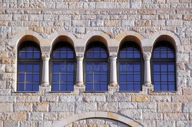 Five old windows with arches, columns and lattices on a stone wa