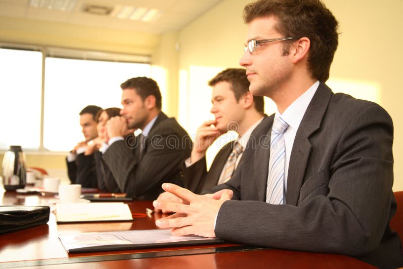 Cinque persone in giacca e cravatta seduto a un tavolo delle conferenze, prendere parte a riunioni e / o la presentazione.