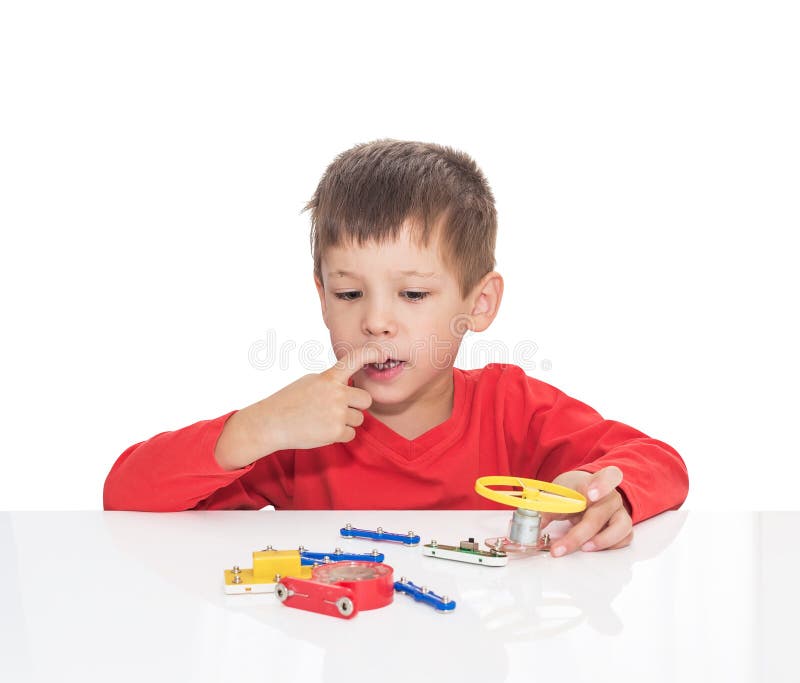 The five-year-old boy sits at a white table and plays an electronic designer