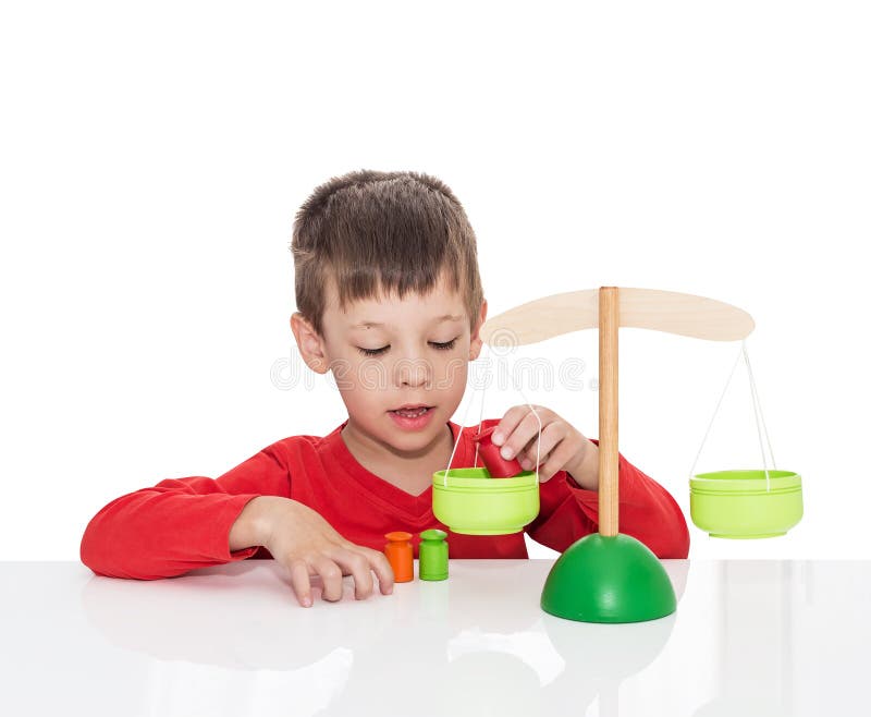 The five-year-old boy sits at a white table and plays with wooden scales