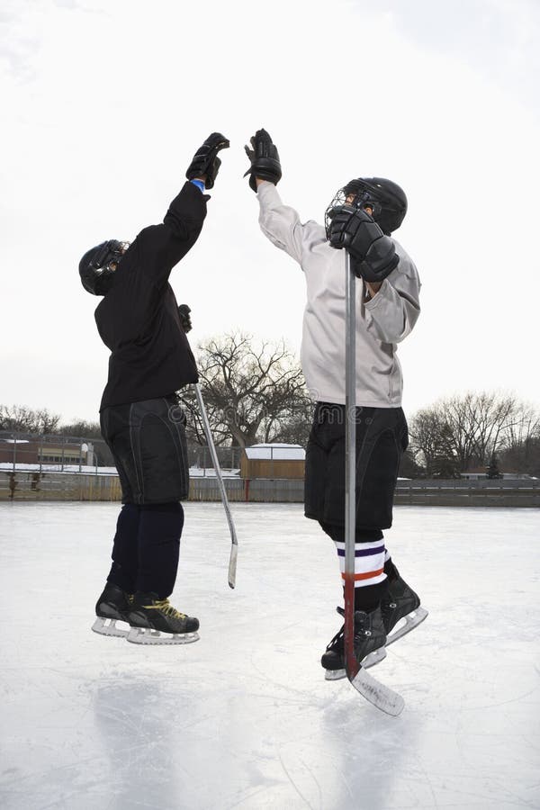 Two boys in ice hockey uniforms giving eachother high five on ice rink. Two boys in ice hockey uniforms giving eachother high five on ice rink.