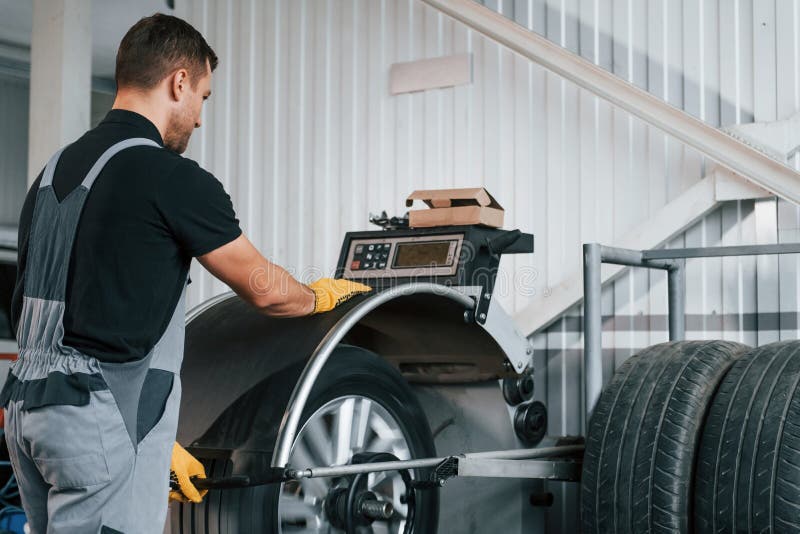 Fixing the Tire. Man in Uniform is Working in the Auto Service Stock