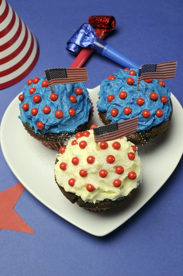 Fourth 4th of July Independence Day party celebration with red, white and blue chocolate cupcakes on white heart plate and USA American flags. Fourth 4th of July Independence Day party celebration with red, white and blue chocolate cupcakes on white heart plate and USA American flags