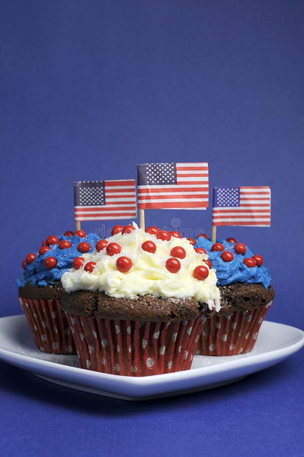 Fourth 4th of July party celebration with red, white and blue chocolate cupcakes on white heart plate and USA American flags. Fourth 4th of July party celebration with red, white and blue chocolate cupcakes on white heart plate and USA American flags