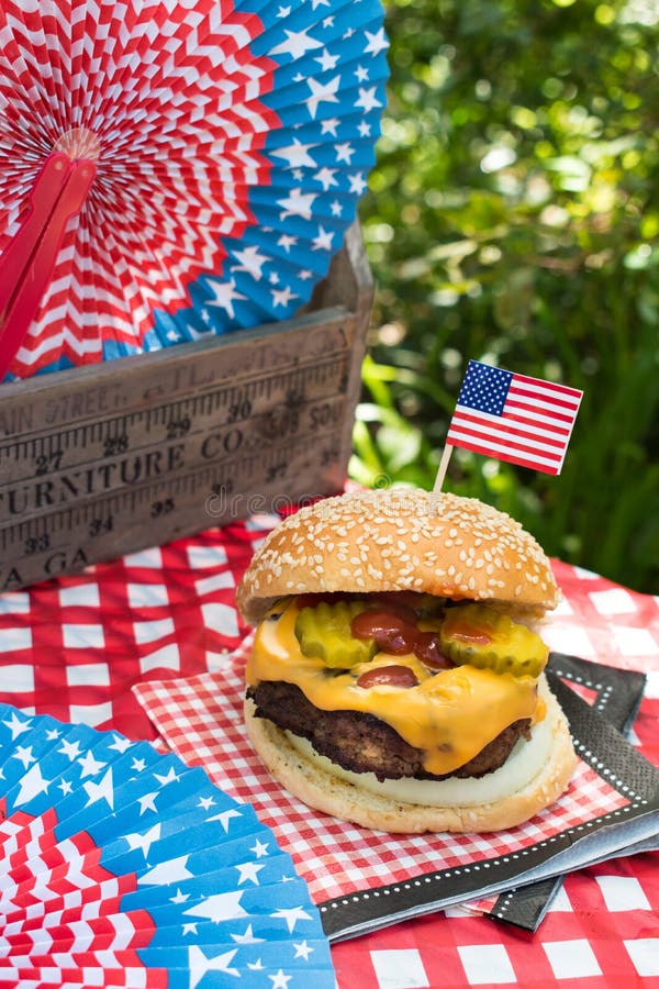 Fourth of July celebration with All American hamburger on outdoor picnic table. Fourth of July celebration with All American hamburger on outdoor picnic table