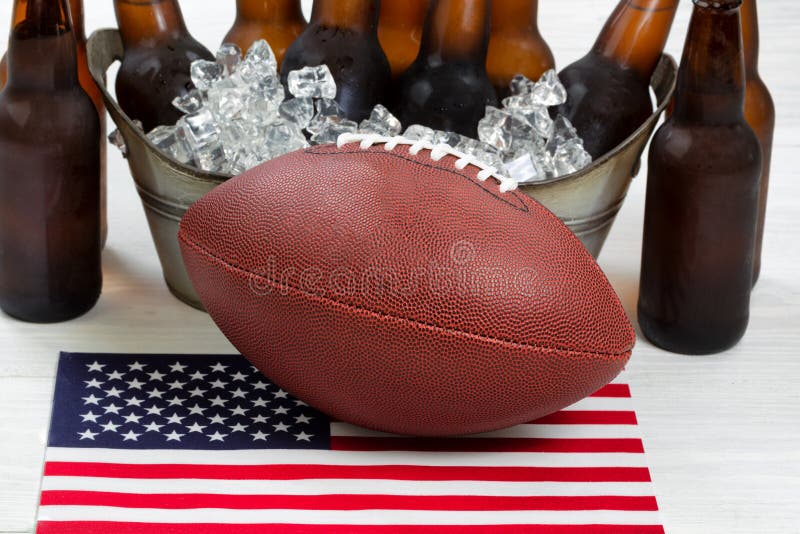 Close up of American football, ice cold beer in bucket, and flag with rustic white wood underneath. Perfect for the Fourth of July holiday. Filled frame in horizontal format. Close up of American football, ice cold beer in bucket, and flag with rustic white wood underneath. Perfect for the Fourth of July holiday. Filled frame in horizontal format.