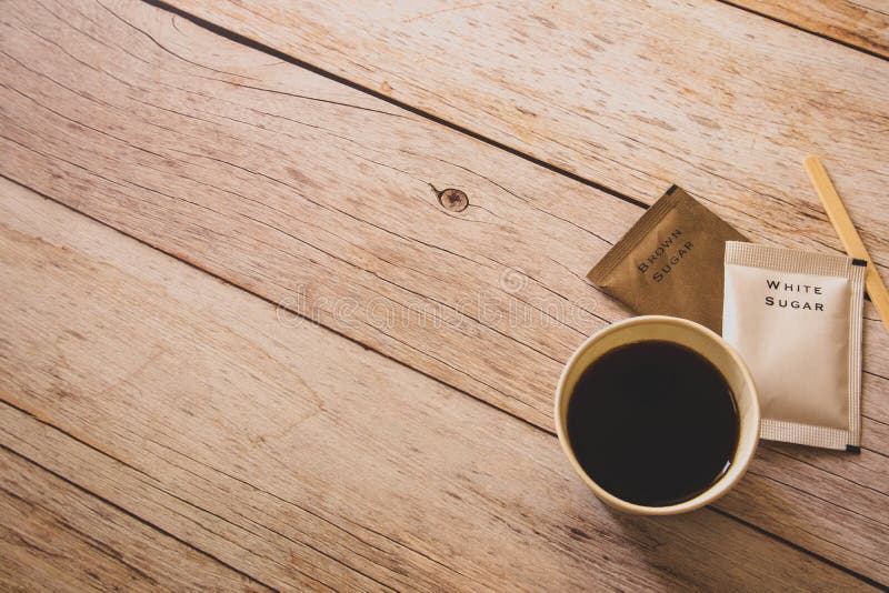 Flache Lage des schwarzen Kaffees in der Weißbuchschale mit weißer und brauner Zuckertaschen und hölzernem Stock auf Holztisch al lizenzfreies stockfoto Flache Lage des schwarzen Kaffees in der Weißbuchschale mit weißer und brauner Zuckertaschen und hölzernem Stock auf Holztisch al lizenzfreies stockfoto