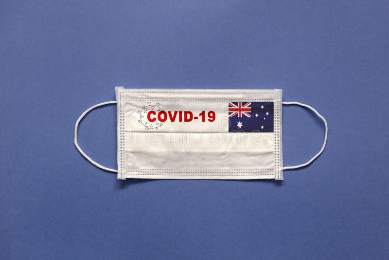 Flag of Australia and inscription COVID-19 on a medical mask on a blue background. Healthcare and medical concept. Pandemic virus COVID-19.