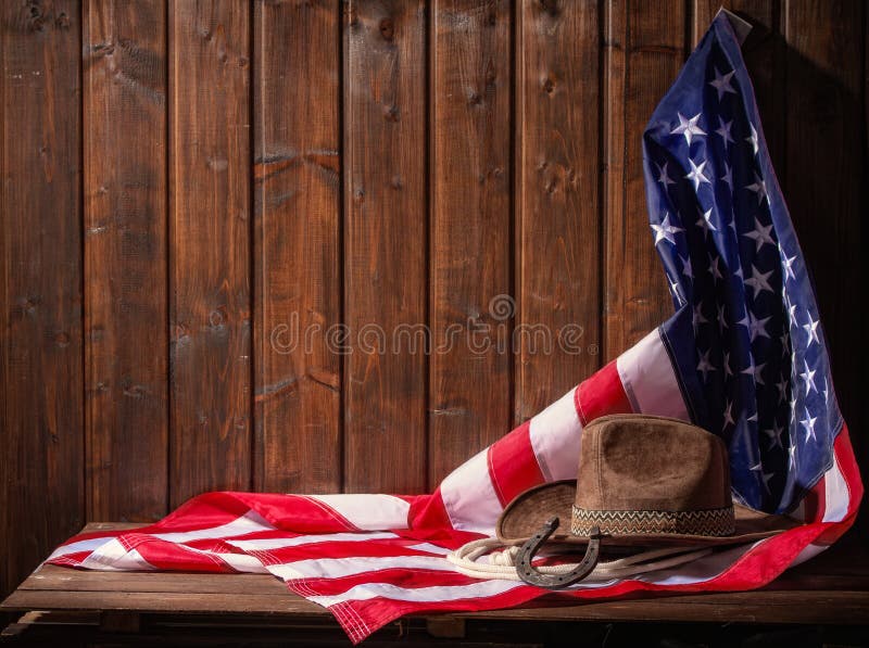 Classic cowboy hat lasso and horseshoe lie on a star-striped USA flag on a dark wooden background. Classic cowboy hat lasso and horseshoe lie on a star-striped USA flag on a dark wooden background