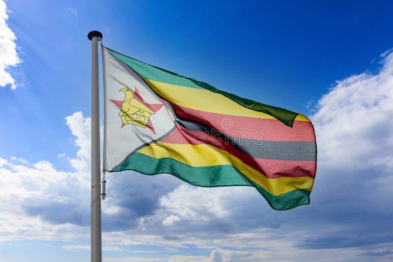 Flaga zimbabwe machająca na niebieskie, chmurowe niebo obrazy stock