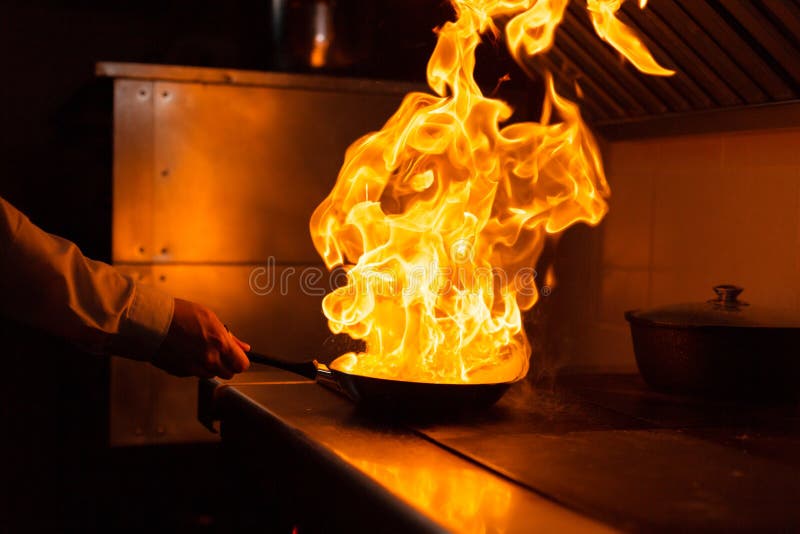 Flambe lamb rib roast. Cooking with fire in frying pan. Professional chef in a commercial kitchen cooking. Man frying. Bone, catering.