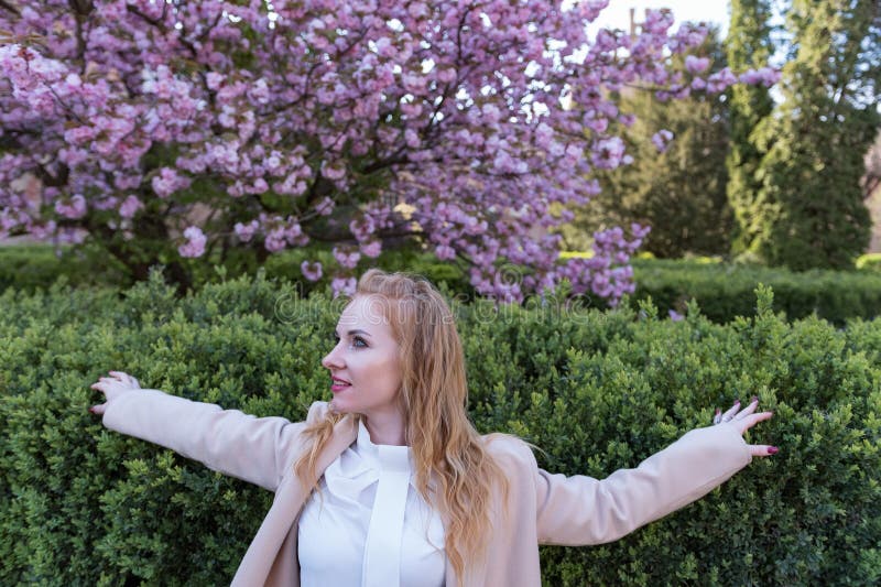 Flamhuggen kvinna i beige-rock mot bakgrund av grön buk. ung kvinna utomhus som blåser sakuradrädet royaltyfria foton