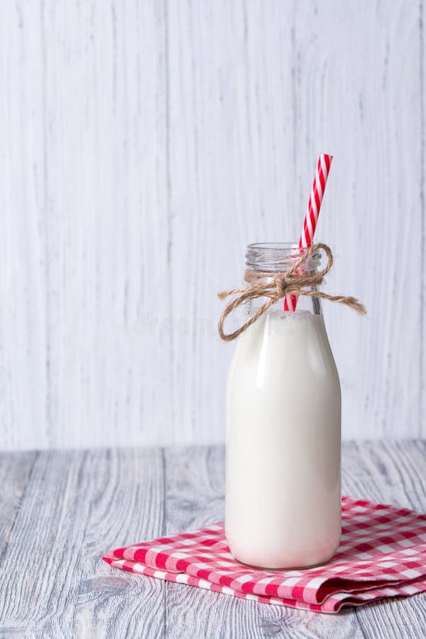 Flasche Milch mit rotem Stroh, hölzerner Hintergrund. Flasche Frischmilch mit rotem gestreiftem Stroh, hölzerner Hintergrund