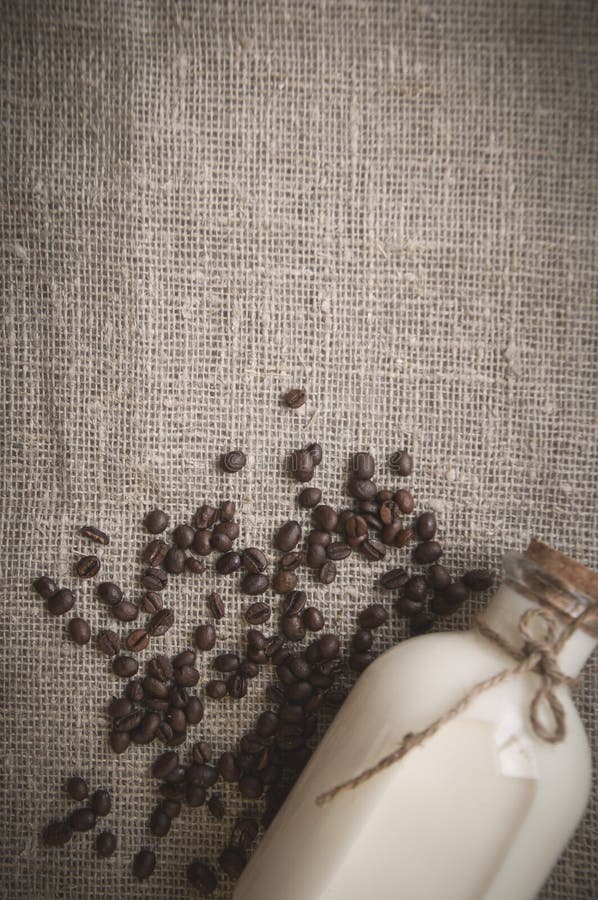 Flaskan av mjölkar och lossar kaffebönor på bakgrund av linne arkivbild Flaskan av mjölkar och lossar kaffebönor på bakgrund av linne arkivbild