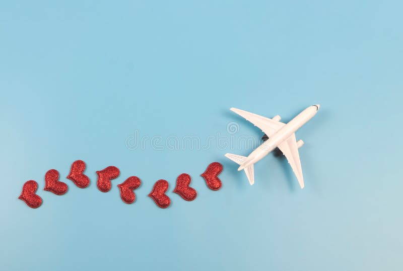 Flat lay of airplane model with red hearts on blue background. Honeymoon trip or travel lover concept