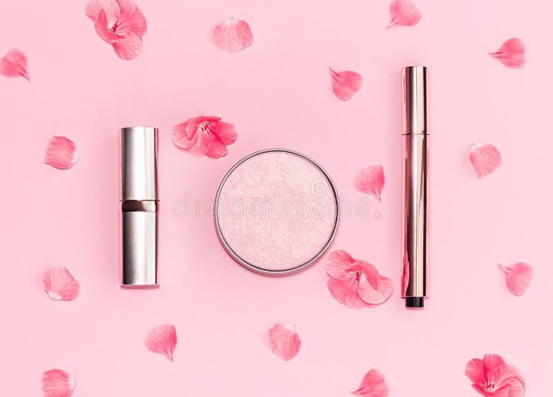 Flat lay composition with decorative makeup products and pink flowers on pastel pink background.