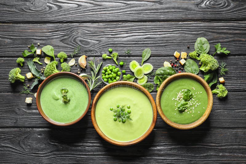 Flat lay composition with different fresh vegetable detox soups made of green peas, broccoli and spinach in dishes on table.