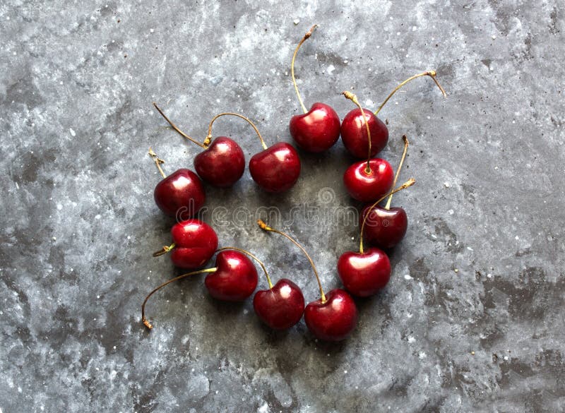 Flat lay composition in hart shape with fresh cherries on dark background. Flat lay pattern, top view. High quality