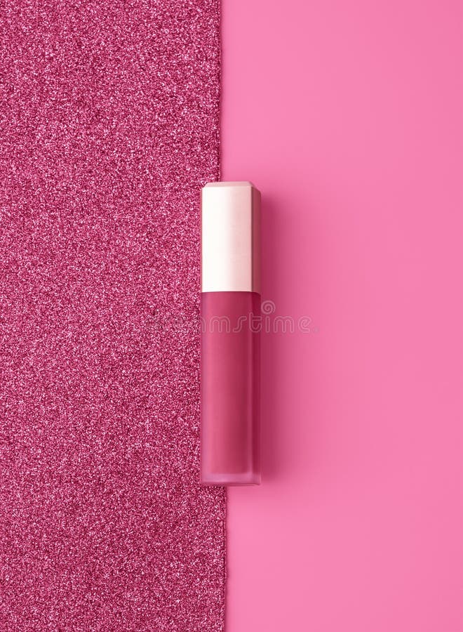 Flat lay composition with vivid pink golden lip gloss on bright pink and sparkling background.