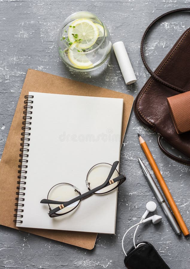 Flat lay female office desk with notepad, tablet, leather bag, glasses, earphones, lipstick and a glass of refreshing lemon thyme stock image