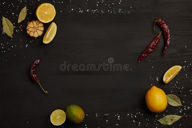 flat lay with lemon and lime pieces, spices, chili peppers and bay leaves on black tabletop