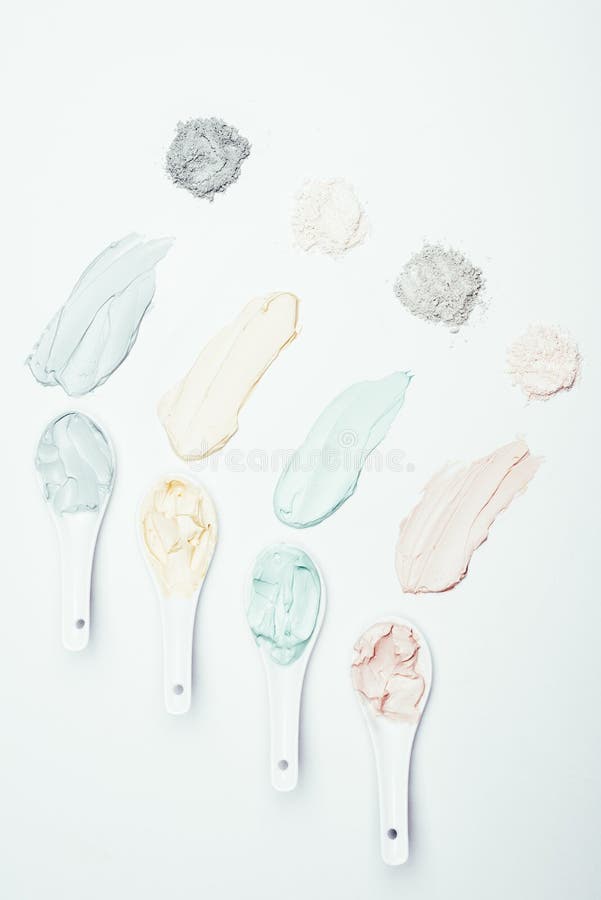 flat lay with spoons, different clay powder and colorful clay mask smudges placed in row