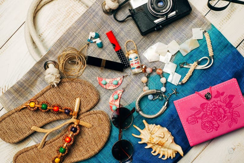 Flat lay of summer fashion with camera, slippers, sunglasses and other girl accessories on top of the bag on white wooden backgrou