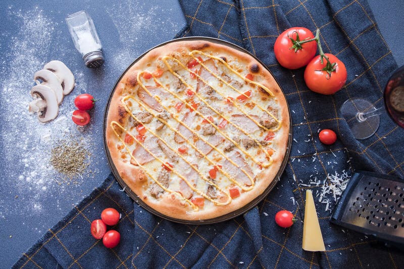 Flat lay with traditional Italian pizza with chiken, ham, pepper, cheese and tomatoes on dark blue stone table and ingredients stock images Flat lay with traditional Italian pizza with chiken, ham, pepper, cheese and tomatoes on dark blue stone table and ingredients stock images