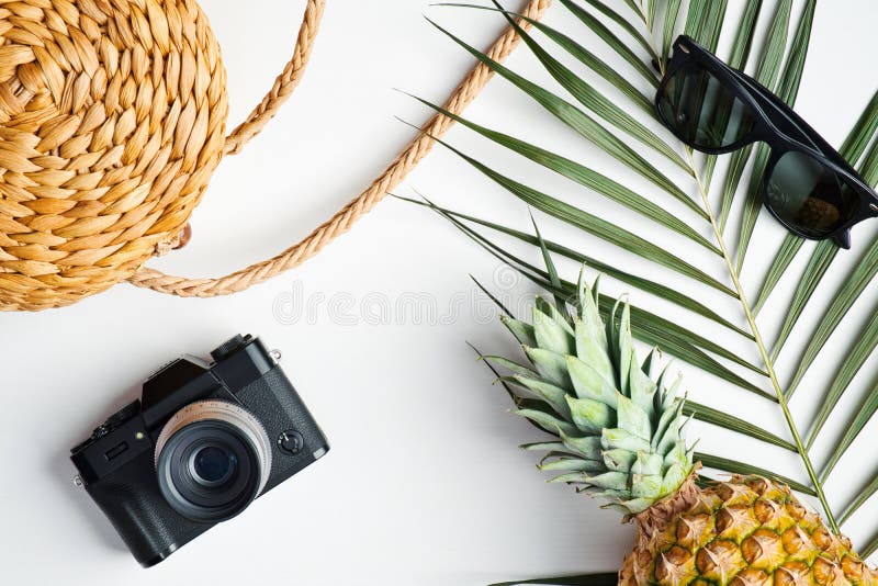 Flat lay traveler accessories with palm leaf on white background. Top view rattan straw bag, vintage camera, sunglasses, pineapple