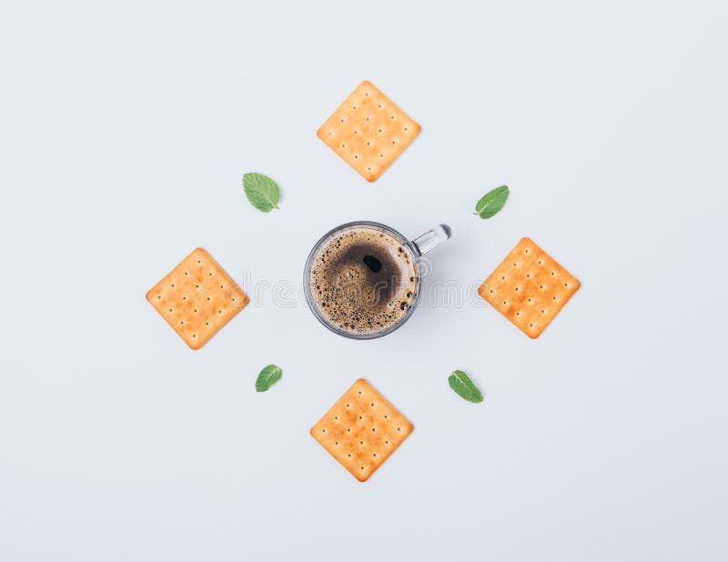 Flat layout of crackers, green leaves and cup of black coffee in center on white background. Top view creative food composition of.