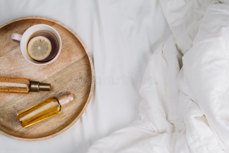 Flatlay of bed with white sheets, blankets and wooden tray with lemon tea and body or hair oils. Or serums, concept of morning or night skincare stock photo Flatlay of bed with white sheets, blankets and wooden tray with lemon tea and body or hair oils. Or serums, concept of morning or night skincare stock photo