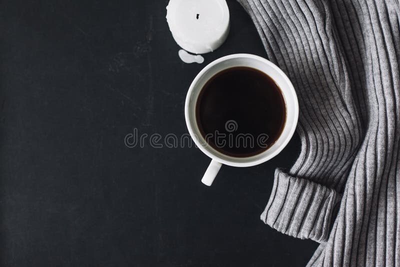 Winter cozy concept. Flatlay of gray knitted sweater, candle and coffee drink on black iron table. Warm weekend in cold weather. Winter cozy concept. Flatlay of gray knitted sweater, candle and coffee drink on black iron table. Warm weekend in cold weather.