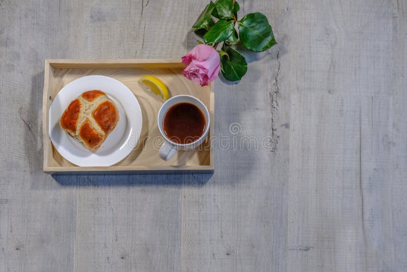 Flatlay ha sparato di un vassoio che tiene una tazza di tè, la fetta di limone e un panino trasversale caldo su un piatto Un osse fotografie stock libere da diritti Flatlay ha sparato di un vassoio che tiene una tazza di tè, la fetta di limone e un panino trasversale caldo su un piatto Un osse fotografie stock libere da diritti
