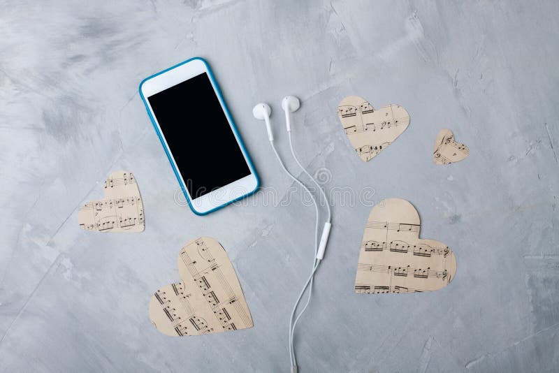 Flatlay composition smartphone or mobile phone, paper hearts, headphones on gray concrete background. Music or technology background. Flatlay, top view. Flatlay composition smartphone or mobile phone, paper hearts, headphones on gray concrete background. Music or technology background. Flatlay, top view.