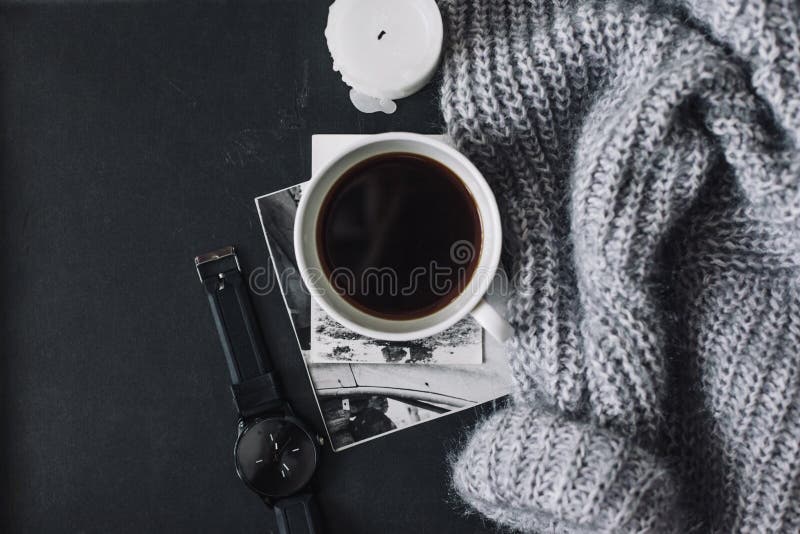 Flatlay of winter sweater and coffee. Winter cozy concept. Flatlay of gray knitted sweater, candle and coffee drink on black iron table. Warm weekend in cold stock photo Flatlay of winter sweater and coffee. Winter cozy concept. Flatlay of gray knitted sweater, candle and coffee drink on black iron table. Warm weekend in cold stock photo