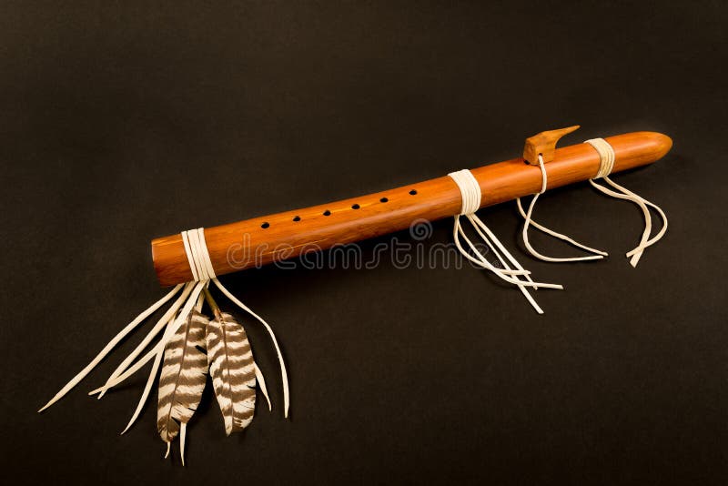 Primitive Antique Native American Flute with Feathers on a Black Background. Primitive Antique Native American Flute with Feathers on a Black Background.