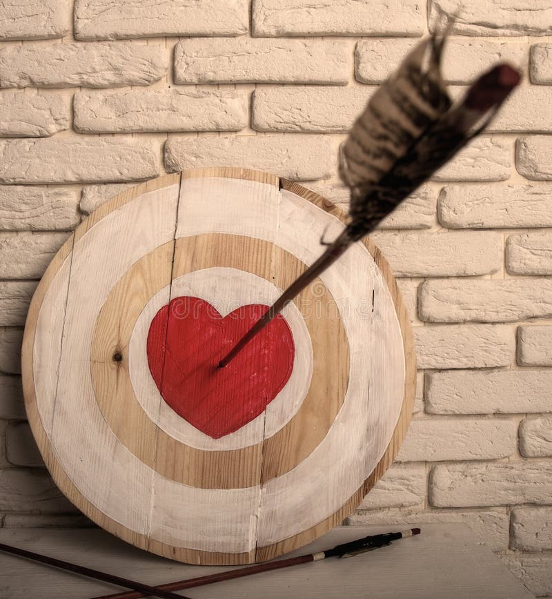 Flecha del coraz? n de la blanco. Handmade rough wooden target with a center in the form of a red heart and an arrow from a bow that hit the center and two arrows missed