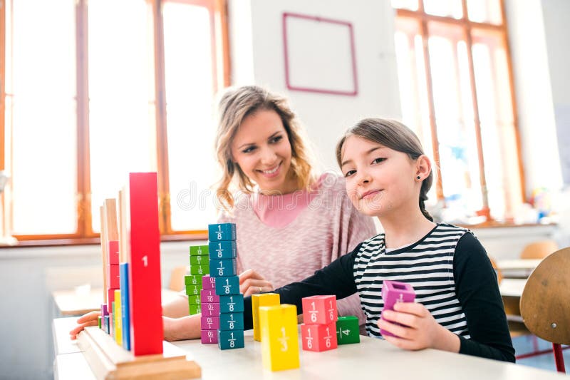 Fleißige Lehrerin lernt mit jungen Schülerinnen im Klassenzimmer, indem sie ihre Brüche mithilfe von Schulwerkzeugen erklärt. stockfotografie